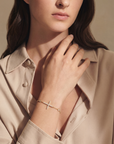 Woman wearing a beige shirt and gold bracelet, with a neutral background