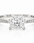 A princess cut diamond engagement ring with a silver-colored band set with pavé diamonds, shown on a clean white background.