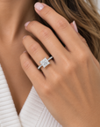 A close-up lifestyle shot of a model's hand wearing a silver-toned diamond ring with a square princess-cut center stone.