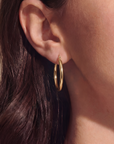 Close-up of a person wearing a gold hoop earring with hair partially obscuring the view.