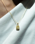 person wearing a gold necklace with a yellow gemstone pendant on a white fabric background