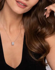 Woman wearing a white gold necklace with a square pendant against a neutral background