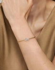 Person wearing a delicate bracelet with a cross charm on a neutral background