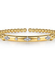 A gold bangle bracelet featuring a central bar adorned with small diamond clusters and circular diamond accents, flanked by a beaded gold band, shown on a clean white background.