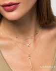 Close-up of a woman wearing a gold necklace with a 'M' pendant, branded 'GABRIEL & CO'.