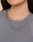 A close-up of a model wearing a two-tone chain necklace with silver and gold links over a gray ribbed tank top.
