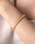 Gold beaded bracelet on a wrist with a neutral background