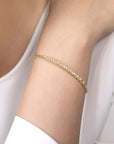 A delicate gold bracelet with small clear stones, shown worn on a person's wrist against a white top.