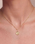 Gold necklace with a cross pendant on a person's neck against a neutral background
