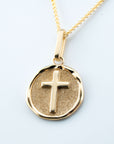 Gold necklace with a round pendant featuring a cross on a light gray background