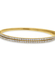 A 14k yellow gold rigid oval bangle bracelet showcasing two parallel rows of brilliant round diamonds across the top half, finished with finely textured vertical engraving along the outer gold edges.