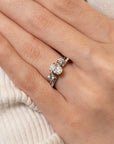 Diamond enhancer ring with oval diamond solitaire on a person's finger with a neutral background