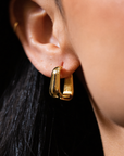 Gold hoop earrings worn by a person with dark hair.
