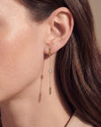 Close-up of a gold earring with a chain and gemstone worn by a person.
