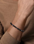 Black beaded bracelet on a wrist with a brown background