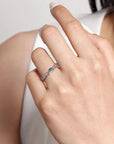 Close-up of a hand wearing a blue stone ring on a neutral background