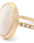 Gold ring with a white mother of pearl stone and diamond-studded band on a white background