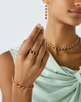 A close-up lifestyle shot of a model wearing gold jewelry, featuring a ring with red gemstones on her finger, a matching beaded necklace, and a bracelet, set against a clean white background.