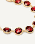 A close-up of a gold chain bracelet featuring round rose-cut, deep red gemstones in gold bezel settings, set against a clean white background.