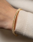yellow gold double flexible tennis bracelet on a wrist with a beige sweater background