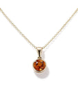 A gold chain necklace with a round shaped pendant featuring a faceted citrine gemstone in a gold bezel setting, shown against a plain white background.