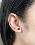 person wearing a yellow gold and garnet stud in their ear