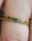 A close-up of a gold ring with small, multi-colored gemstones set on a person's finger.