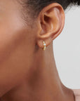 Close-up of an ear wearing a gold hoop earring against a neutral background