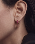 Close-up of an ear wearing a small hoop earring with pink gemstones.
