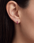 Close-up of an ear wearing a yellow gold and ruby hoop earring with dark hair.
