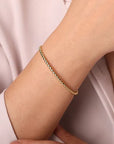Gold bracelet on a person's wrist with a light pink background