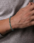 Hand wearing a green 4mm beaded bracelet on a gray background