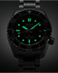 Black Seiko watch with green glowing face on a dark background
