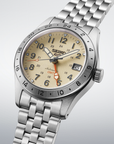 A Seiko wristwatch with a stainless steel link bracelet, featuring a beige dial with black Arabic numerals, a silver bezel, and a date window.- angled