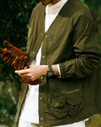 Person wearing a green jacket holding brown gloves with a blurred green background
