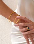 Gold bracelet and ring on a person's wrist and finger against a white background