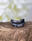 Two black rings with silver accents on a wooden surface with a blurred natural background