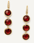 A pair of gold drop earrings featuring three faceted round red gemstones in each earring, accented with small clear stones along the top hooks, set against a plain off-white background.
