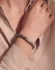 close up of an arm with a gold and black swirled bracelet with embedded diamonds on a beige background