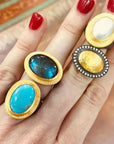 Four rings with different colored stones on a hand with red nail polish.