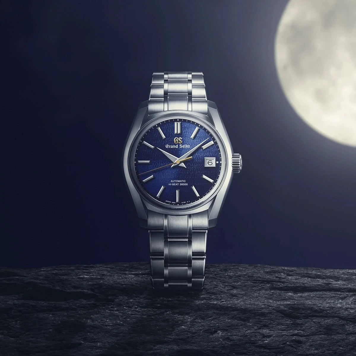 Silver watch with blue dial on a dark surface with moon in the background