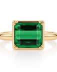 An green gemstone ring set in a polished yellow gold bezel with prongs with a matching gold band, shown on a clean white background with a soft reflection.
