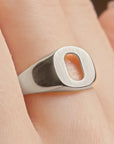 A close-up of a silver signet ring with a rectangular face and an oval cutout, worn on a finger.