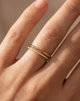 Close-up of a hand wearing a gold ring with diamond accents on a neutral background