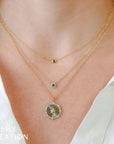 Two gold necklaces with green gemstones and one with a medallion on a person wearing a white top, branded 'SHY CREATION'.