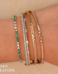 Three gold bracelets with green gemstones, clear stones, and black stones on a wrist, with 'SHY CREATION' branding.