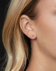 Close-up of an ear wearing a gold stud earring with blonde hair.