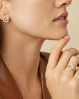 Close-up of a woman wearing silver tone and gold hoop earrings and a ring on a beige background
