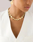 Woman wearing a gold necklace and earrings against a neutral background