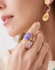 Close-up of a woman's hand wearing a gold ring with purple and pink stones, and gold earrings.